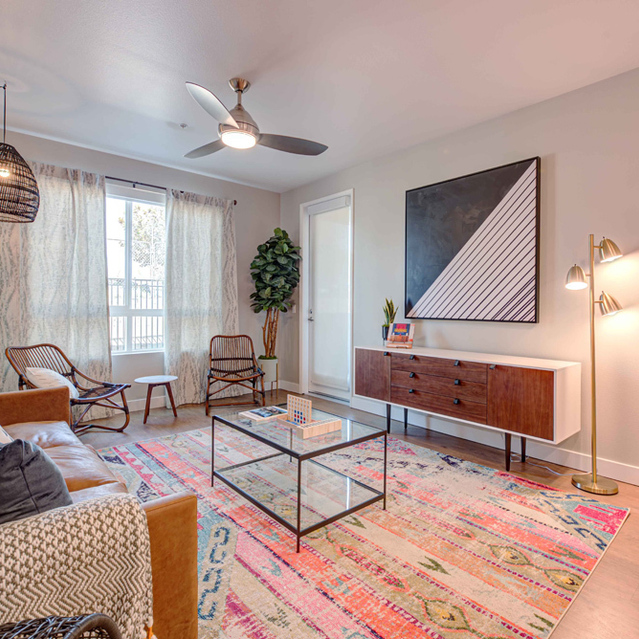 Dog-Friendly Apartments in Redlands, CA - The Summit - Living Room With Contemporary Plank Flooring, Area Rug, Ceiling Fan, Floor Lamps, Leather Couch, Glass Coffee Table, and Large Window